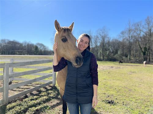 Kate smiles to camera with a horse.
